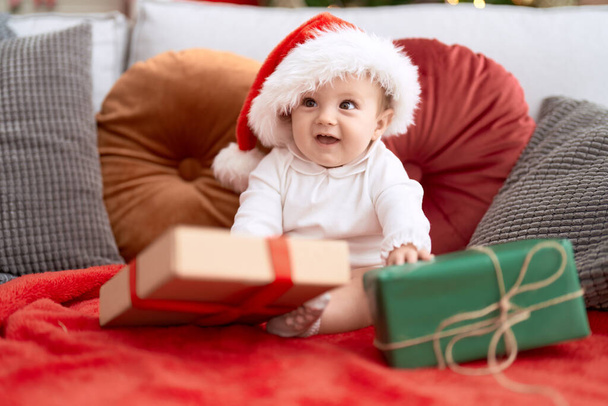 Adorable toddler wearing christmas hat sitting on sofa with present at home - Foto, Bild
