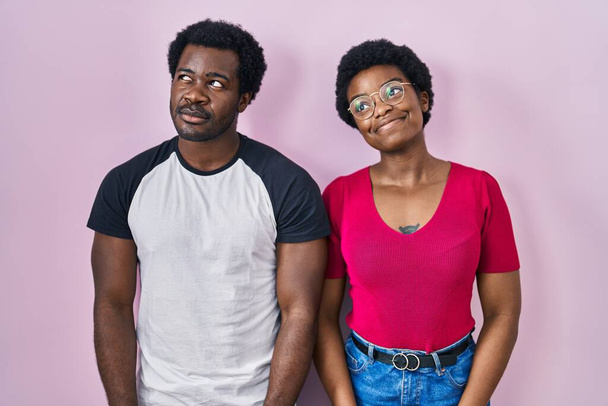 Giovane coppia afro-americana in piedi sopra sfondo rosa sorridente guardando di lato e fissando via pensando.  - Foto, immagini
