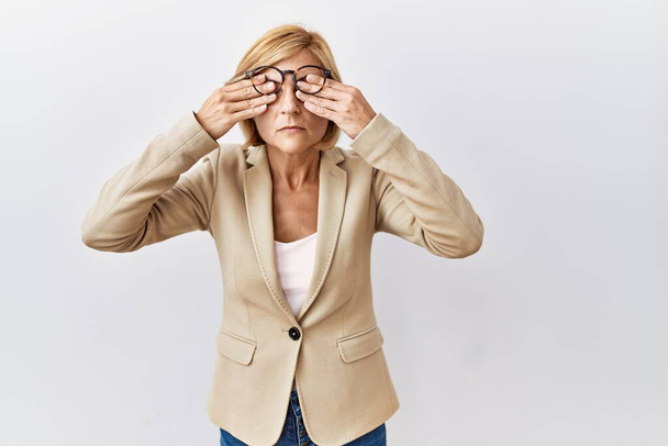Блондинка середнього віку бізнес-леді стоїть над ізольованим тлом, натираючи очі на втому і головний біль, сонний і втомлений вираз. проблема зір
  - Фото, зображення