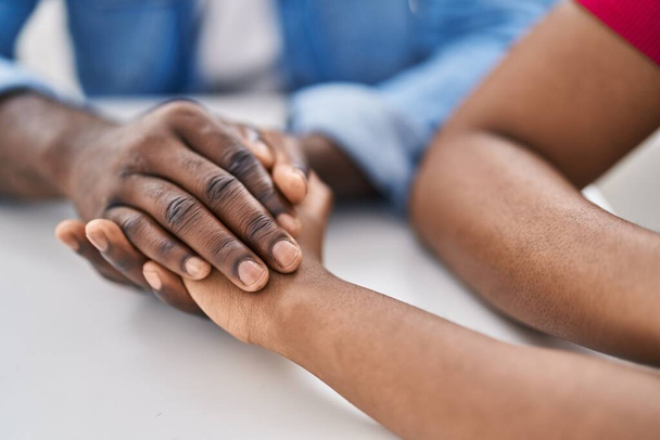 Africano americano hombre y mujer pareja sentado en mesa con las manos juntas en casa - Foto, Imagen