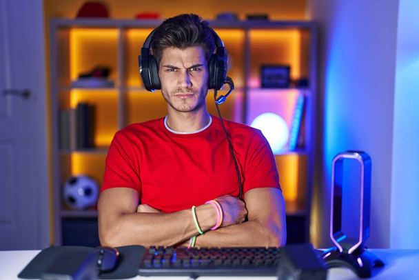 Jovem hispânico jogando videogames cético e nervoso, desaprovando a expressão no rosto com os braços cruzados. pessoa negativa.  - Foto, Imagem