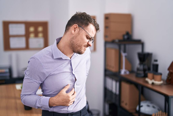 Junger hispanischer Mann im Büro leidet unter Nackenschmerzen, Berührung des Nackens mit der Hand, Muskelschmerzen  - Foto, Bild