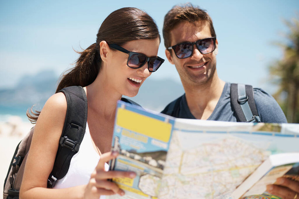 Wie kamen wir ins Paradies? ein junges Paar blickt auf eine Landkarte, während es am Strand steht - Foto, Bild