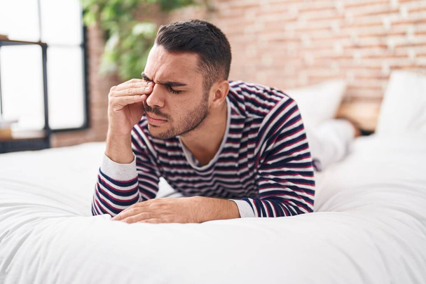 Jonge Spaanse man gestrest liggend op bed in de slaapkamer - Foto, afbeelding