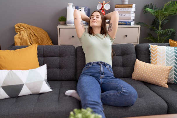 Young beautiful woman relaxed with hands on head sitting on sofa at home - Photo, Image