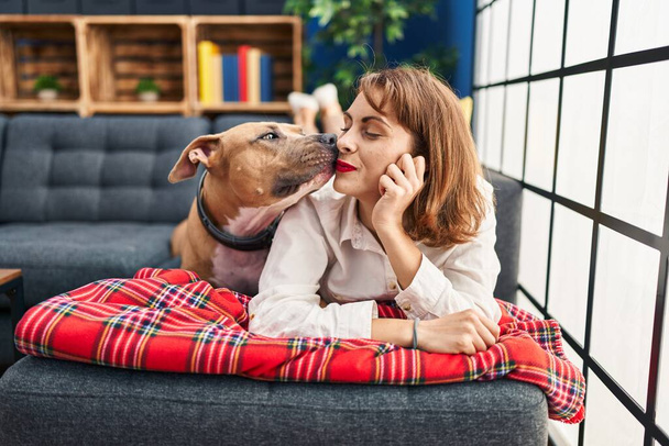 Joven mujer caucásica sonriendo confiado acostado en sofá con perro en casa - Foto, imagen