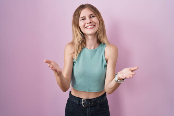 Blonde caucasian woman standing over pink background smiling cheerful offering hands giving assistance and acceptance.  - Foto, immagini