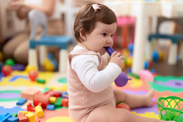 Adorable toddler bitting plastic food toy sitting on floor at kindergarten - Photo, image