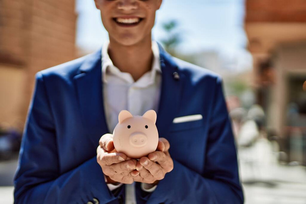 Young man wearing suit holding piggy bank at street - Foto, Imagen