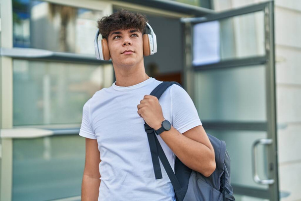 Νέος Ισπανόφωνος έφηβος φοιτητής χαμογελά σίγουρος ακούγοντας μουσική στο πανεπιστήμιο - Φωτογραφία, εικόνα