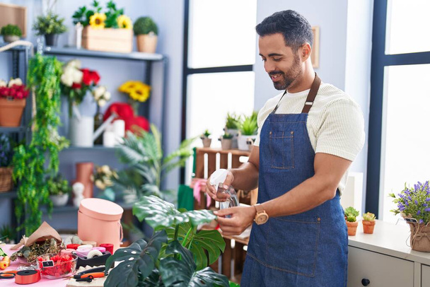 Young hispanic man florist smiling confident watering plant at florist - Photo, Image