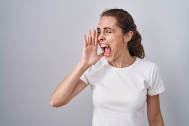 Beautiful brunette woman standing over isolated background shouting and screaming loud to side with hand on mouth. communication concept.  - Photo, Image