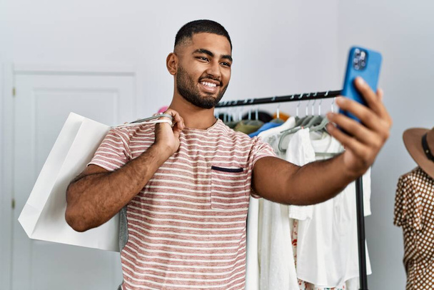 Νεαρός Άραβας κάνει selfie από το smartphone κρατώντας τσάντες ψώνια στο κατάστημα ρούχων - Φωτογραφία, εικόνα
