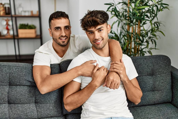 Dois homens hispânicos casal sorrindo confiante e abraçando uns aos outros em casa - Foto, Imagem