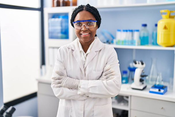 Afrykańska Amerykanka naukowiec uśmiecha się pewnie stojąc z ramionami skrzyżowane gest w laboratorium - Zdjęcie, obraz
