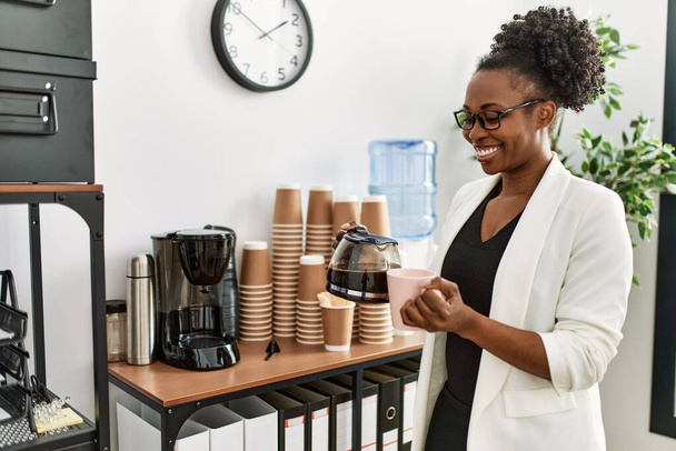 Африканская американка-бизнес-работница наливает кофе на чашку кофе в офисе - Фото, изображение