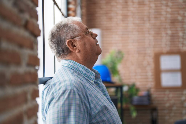 Middelbare leeftijd grijsharige man zakenman gestrest staande op kantoor - Foto, afbeelding