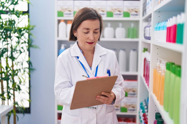 Middle age woman pharmacist writing on document at pharmacy - Photo, Image