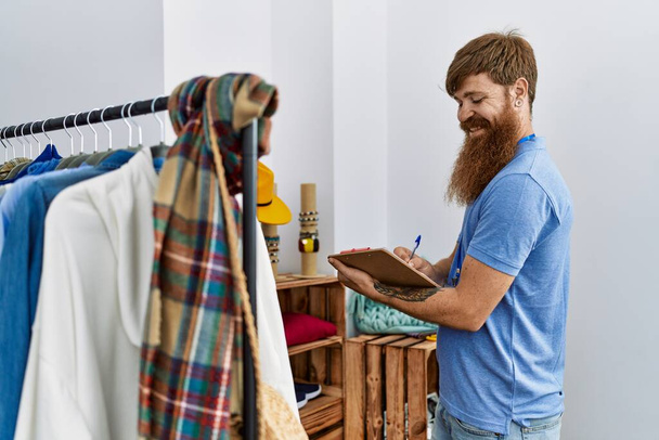 Молодой ирландский торговец улыбается счастливо работая в магазине одежды. - Фото, изображение