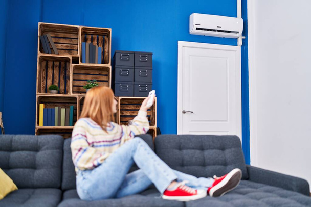 Nuori valkoihoinen nainen käyttää ilmastointi kone istuu sohvalla kotona - Valokuva, kuva