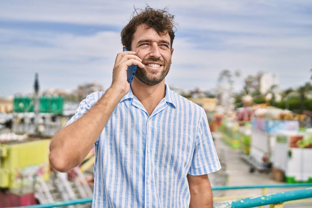 Junger hispanischer Mann lächelt glücklich und spricht auf dem Smartphone im Freizeitpark. - Foto, Bild