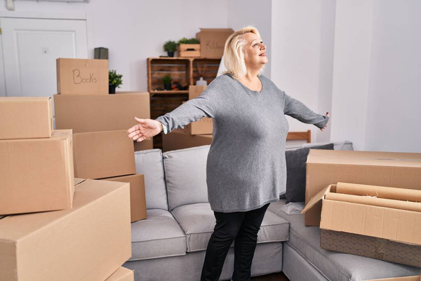 Middle age blonde woman breathing with arms open standing at new home - Photo, Image