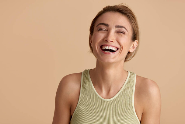 Beauty Woman Laughing Isolated Portrait. Blonde Woman Model With Smooth Skin Smiling Against Beige Background. Confident Female Enjoying Her Perfect Body After Cosmetology Treatment  - 写真・画像