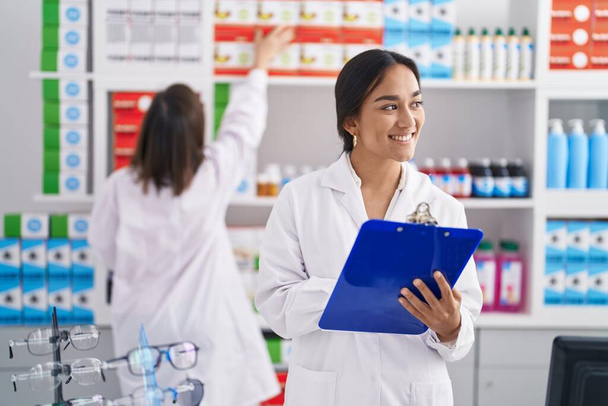 Two women pharmacist smiling confident writing on document at pharmacy - Zdjęcie, obraz