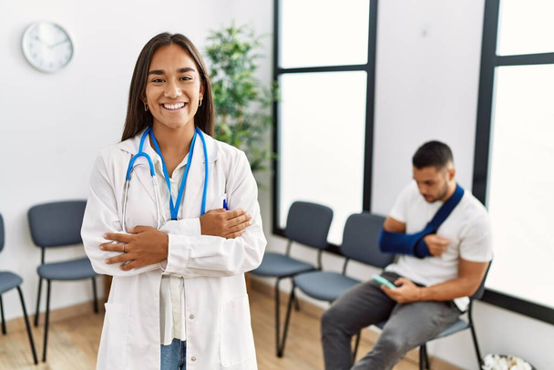 Young asian doctor woman at waiting room with a man with a broken arm happy face smiling with crossed arms looking at the camera. positive person.  - Photo, Image