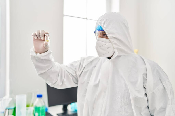 Científico joven latino usando protección covid uniforme sosteniendo dosis de vacuna en laboratorio - Foto, imagen