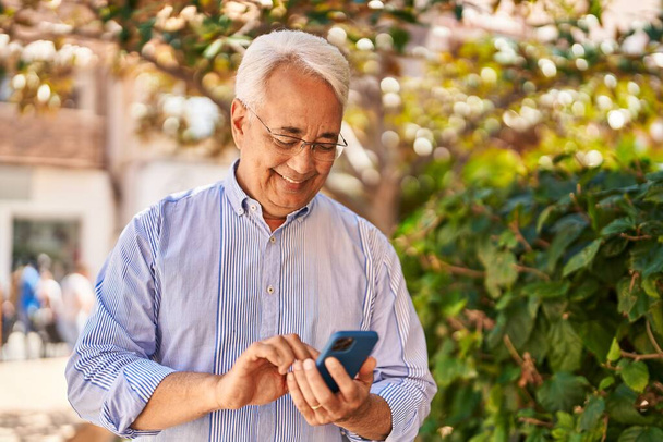 Senior man smiling confident using smartphone at park - 写真・画像