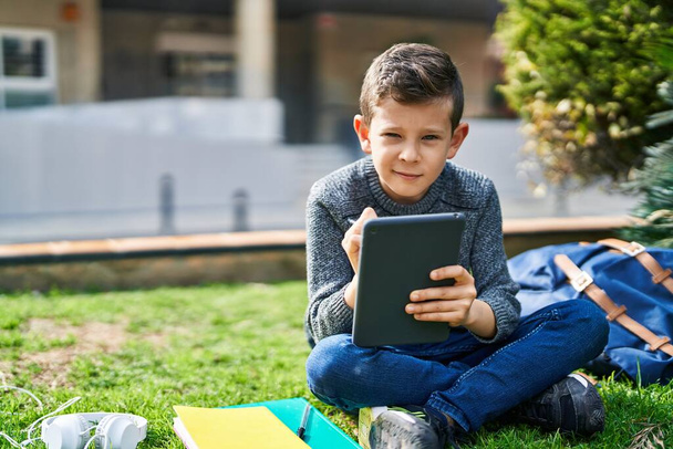 Blondes Kind sitzt mit Touchpad im Park auf Gras - Foto, Bild