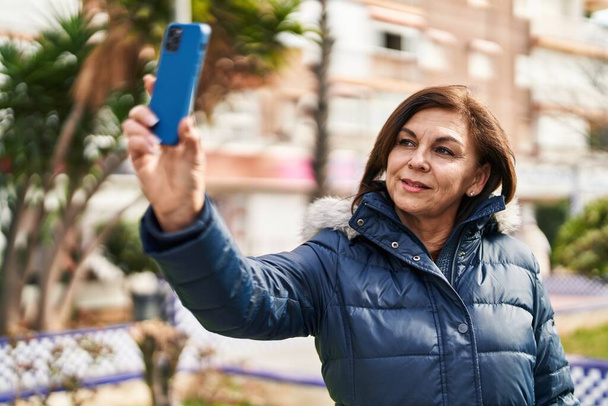 Frau mittleren Alters lächelt selbstbewusst und macht Selfie mit dem Smartphone auf der Straße - Foto, Bild