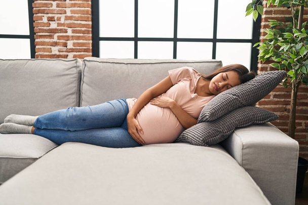 Mujer latina joven embarazada durmiendo en el sofá en casa - Foto, Imagen