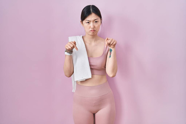 Čínská mladá žena ve sportovním oblečení a ručníku ukazuje dolů vypadá smutně a rozrušeně, ukazuje na směr s prsty, nešťastné a depresivní.  - Fotografie, Obrázek