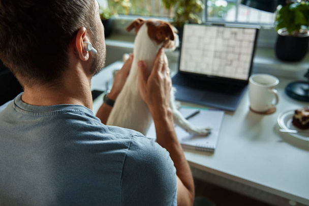 Freelancer työskentelee kotona koiran kanssa. Nainen käyttää kannettavaa tietokonetta ja kirjoittaa muistioon istuu pöydässä kotitoimistossa. - Valokuva, kuva