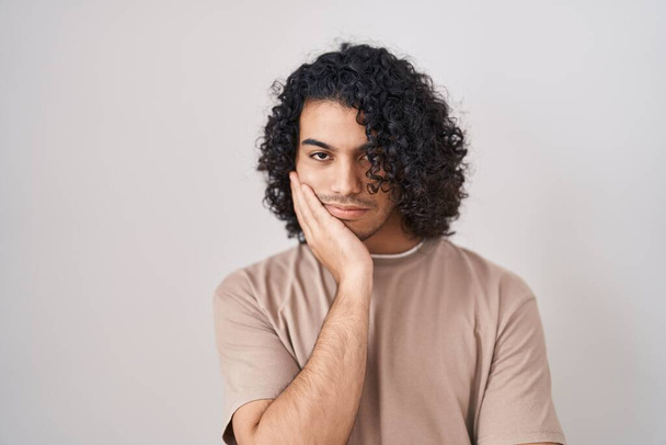 Latino mies kihara tukka seisoo valkoinen tausta ajattelu näyttää väsynyt ja kyllästynyt masennus ongelmia ristissä kädet.  - Valokuva, kuva