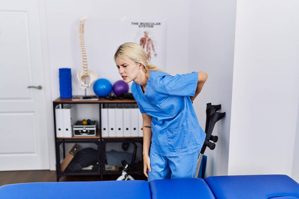 若い理学療法士の女性は、腰痛の回復クリニックで働いています,手で背中に触れて,筋肉痛  - 写真・画像