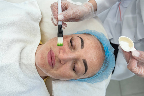 esteticista aplica uma máscara no rosto do paciente com escovas cosméticas enquanto se deita. Esteticista de cosmetologia. procedimentos de beleza - Foto, Imagem
