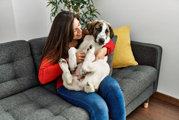 Young woman hugging dog sitting on sofa at home - Foto, Bild