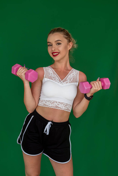 lady in sportswear holding dumbbells and smiling on plain background. The concept of a girl's sports shoot - Photo, Image