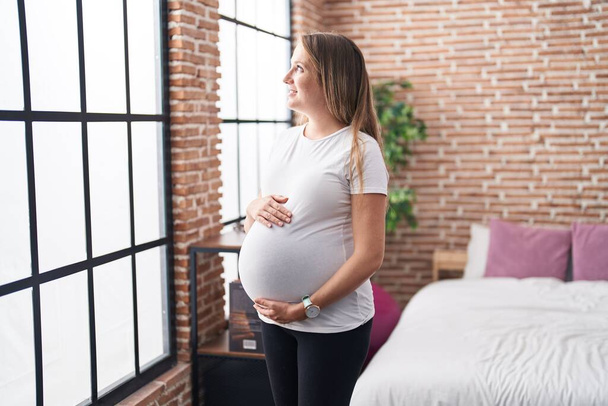 Young pregnant woman smiling confident touching belly standing at bedroom - Φωτογραφία, εικόνα