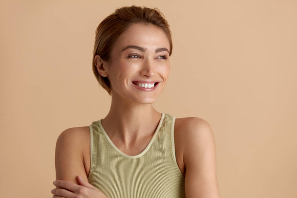 Beauty Woman Posing Isolated Portrait. Blonde Woman Model With Smooth Skin Smiling Against Beige Background. Confident Female Enjoying Her Perfect Body After Cosmetology Treatment  - Φωτογραφία, εικόνα