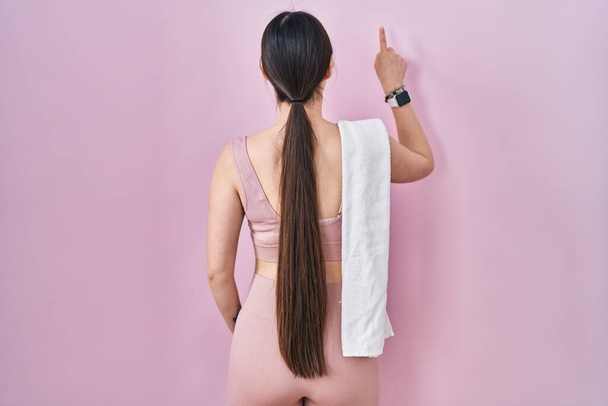 Κινέζα νεαρή γυναίκα φορώντας αθλητικά ρούχα και πετσέτα ποζάρουν προς τα πίσω δείχνοντας προς τα εμπρός με το χέρι δάχτυλο  - Φωτογραφία, εικόνα