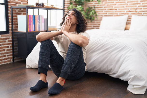 Young latin man stressed sitting on floor at bedroom - Photo, Image