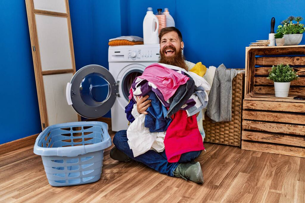 Zrzka muž s dlouhým vousem uvedení špinavé prádlo do pračky mrkání na kameru se sexy výraz, veselý a šťastný obličej.  - Fotografie, Obrázek