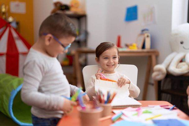 Entzückende Mädchen und Jungen sitzen im Kindergarten auf Tischpapier - Foto, Bild