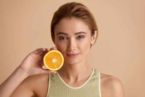 Beautiful Woman Smiling with Orange Fruit. Positive Woman with Radiant Face Recommended Vitamin for Skin. Girl Model with Natural Makeup and Glowing Hydrated Skin. Vitamin C Cosmetics Concept  - Φωτογραφία, εικόνα
