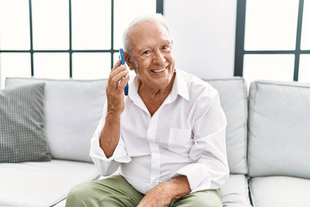 Senior man smiling confident using smartphone at home - Фото, изображение