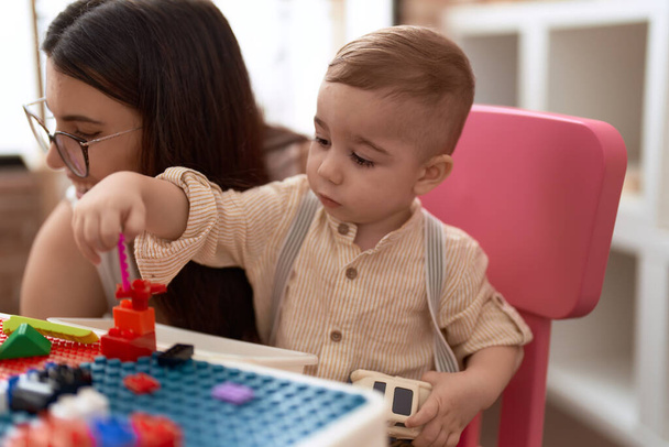 Учитель и дошкольник играют со строительными блоками, сидя за столом в детском саду - Фото, изображение